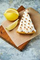 un morceau de tarte au citron décoré d'une tranche de citron sur une planche de bois