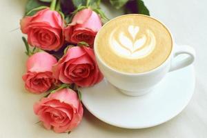 Cappuccino dans une tasse blanche avec cinq roses sur fond de papier photo