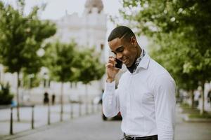 Jeune homme d'affaires afro-américain à l'aide d'un téléphone mobile en attendant un taxi dans une rue photo