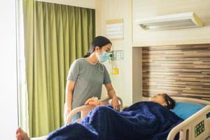 Fille en masque médical visitant sa mère couchée dans son lit à l'hôpital photo