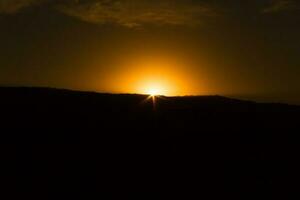 noir silhouette de le montagnes à le coucher du soleil avec d'or ciel photo