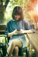 asiatique adolescent séance à Accueil vivant pièce en train de lire message dans intelligent téléphone avec bonheur visage photo