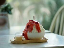 rasé la glace avec fraise sirop et lait, tasse de sucré glace. cool nourriture dessert dans blanc bol sur en bois plateau photo