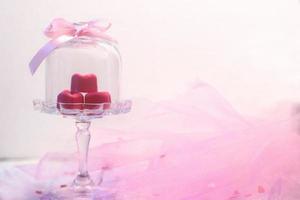 Pralines au chocolat rose en forme de coeur dans une belle cloche en verre sur fond de bois blanc avec espace copie