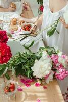 le cuisine plan de travail est décoré avec pivoines. rose pivoines et sucré petits gâteaux sur en bois plan de travail photo