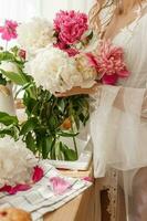 le cuisine plan de travail est décoré avec pivoines. le intérieur est décoré avec printemps fleurs. rose pivoines et sucré petits gâteaux sur une en bois comptoir. intérieur détails. photo