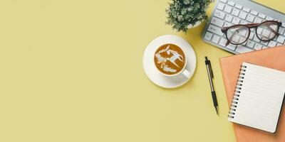 Haut voir, Jaune Bureau bureau avec clavier ordinateur, tasse de café, stylo, monocle et carnet de notes, copie espace, moquer en haut. photo