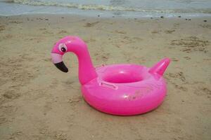 une rose en forme de flamant rose bouée sur le plage sable. été concept photo