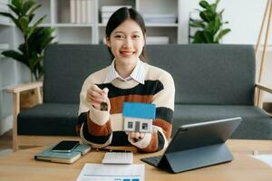 Jeune réel biens agent ouvrier travail avec portable et tablette à table dans Accueil Bureau et petit maison à côté de il. photo