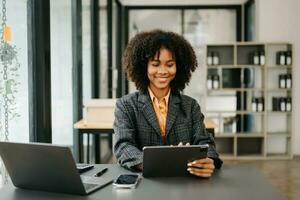 sur de soi africain femme avec une sourire permanent en portant bloc-notes et tablette à le bureau. photo