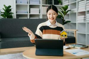 Jeune réel biens agent ouvrier travail avec portable et tablette à table dans Accueil Bureau et petit maison à côté de il. photo