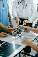 médical équipe ayant une réunion avec médecins dans blanc laboratoire manteaux et chirurgical gommages assise à une table discuter une les patients travail en ligne en utilisant des ordinateurs dans le médical industrie photo