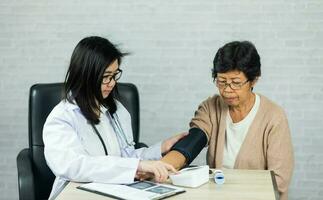 femme médecin mesure du sang pression pour personnes âgées femelle patient sur le médecins Bureau bureau. personnes âgées femelle patient Souffrance de hypertension vérification pour maladie dans hôpital. santé vérifier en haut. photo