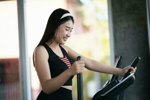 asiatique sportive exercice sur elliptique machine dans le salle de sport, détermination à cardio perdre lester, fait du sa en bonne santé. exercice elliptique machine femme aptitude sport concept. photo