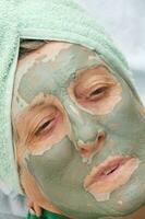 une senior visage est couvert par argile faciale masque.fermer en haut photo