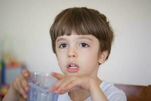 garçon de six ans est prise une verre de chaud Lait avec avoine des biscuits. photo