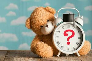 question marque représenté sur une ancien l'horloge avec académique casquette. marron peluche nounours ours dans le Contexte. photo