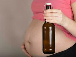 Jeune Enceinte femme garde verre bouteille de Bière proche à sa ventre. photo