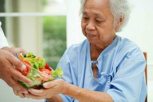 asiatique personnes âgées femme patient en mangeant Saumon pieu et légume salade pour en bonne santé nourriture dans hôpital. photo