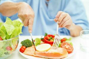 asiatique personnes âgées femme patient en mangeant Saumon pieu et légume salade pour en bonne santé nourriture dans hôpital. photo