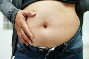 femme asiatique montre gros ventre grande taille surpoids et obésité au bureau. photo