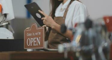 Bienvenue. ouvert. barman, serveuse femme tournant ouvert signe planche sur verre porte dans moderne café café magasin prêt à service, café restaurant, vente au détail magasin, petit affaires propriétaire, nourriture et boisson concept photo