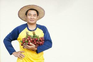 Beau asiatique homme agriculteur porte chapeau, Jaune chemise, détient litchi des fruits. concept, agriculture profession. thaïlandais Les agriculteurs grandir biologique litchis comme un exportation produit de Thaïlande. photo