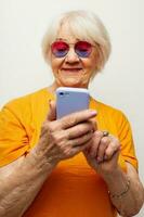 personnes âgées femme dans décontractée T-shirt des lunettes de soleil parlant sur le téléphone isolé Contexte photo