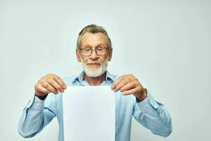 vieux homme dans une bleu chemise et des lunettes une blanc feuille de papier lumière Contexte photo