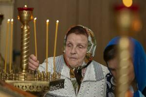 russe grand-mère dans une foulard lumières une bougie dans une église. un personnes âgées femme dans un orthodoxe église. photo