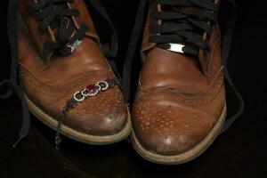 une paire de marron ancien cuir des chaussures avec une pierre bracelet sur une foncé Contexte. magnifique cuir chaussures. rétro chaussures. photo