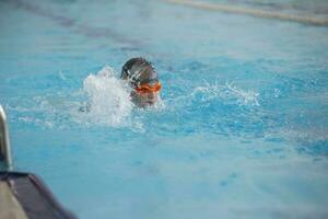 une garçon dans une nager casquette et des lunettes est nager dans le des sports bassin. photo