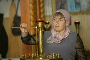 une russe femme dans une foulard lumières une bougie dans le église. photo
