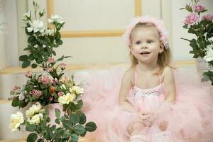 deux ans enfant. une magnifique peu fille dans une intelligent rose robe est assis sur le porche. photo