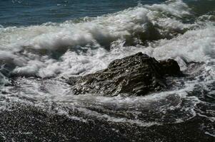 une grand pierre dans Azur eau de mer fermer. une image de le mer le surf. océan le surf parmi le rochers. Contexte de le marée. mer mousse photo