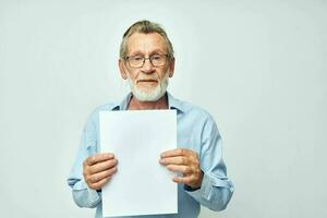 portrait personnes âgées homme dans une bleu chemise et des lunettes une blanc feuille de papier inchangé photo