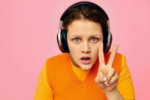 portrait de une Jeune femme écoute à la musique avec écouteurs Orange chandail émotions amusement isolé arrière-plans inchangé photo