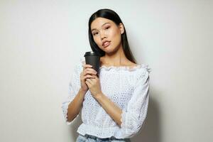 charmant Jeune asiatique femme une noir verre dans le mains de une boisson comme une sourire isolé Contexte inchangé photo