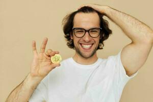 de bonne humeur homme dans une blanc T-shirt avec bitcoin crypto-monnaie beige Contexte photo