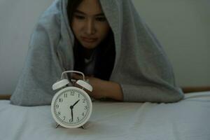 asiatique femme dans lit en retard en essayant à sommeil Souffrance insomnie, sans sommeil ou effrayé dans une cauchemar, à la recherche triste inquiet et stressé. fatigué et mal de crâne ou migraine veille en haut dans le milieu de le nuit. photo