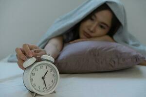 asiatique femme dans lit en retard en essayant à sommeil Souffrance insomnie, sans sommeil ou effrayé dans une cauchemar, à la recherche triste inquiet et stressé. fatigué et mal de crâne ou migraine veille en haut dans le milieu de le nuit. photo