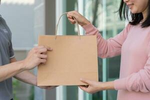 une femme asiatique souriante et heureuse reçoit un colis de nourriture en sac en papier de la maison de messagerie. livreur envoyer livrer express. achats en ligne, conteneur en papier, plats à emporter, facteur, service de livraison, colis photo