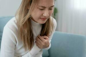 main tenir poitrine avec cœur attaque symptômes, asiatique femme avoir poitrine douleur causé par cœur maladie, fuir, dilatation, agrandi coronaire cœur, presse sur le poitrine avec une douloureux expressi photo