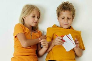 deux joyeux les enfants mensonge sur le sol avec blocs-notes et des crayons isolé Contexte inchangé photo