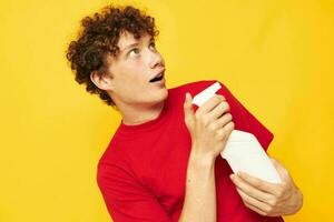 mignonne roux gars dans une rouge T-shirt détergents dans mains posant Jaune Contexte inchangé photo