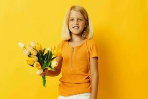 peu fille avec blond cheveux avec une bouquet de Jaune fleurs sur une Jaune Contexte photo