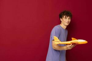 une Jeune homme avec une jouet avion dans une violet T-shirt rouge Contexte inchangé photo