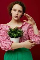 Jeune femme dans rose chemisier est posant avec une plante dans blanc pot fermer photo