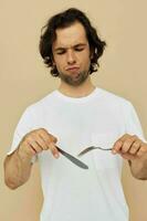 attrayant homme dans une blanc T-shirt avec couteau avec fourchette isolé Contexte photo