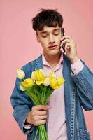 Jeune gars dans une denim veste avec une bouquet de fleurs parlant sur le téléphone rose Contexte photo